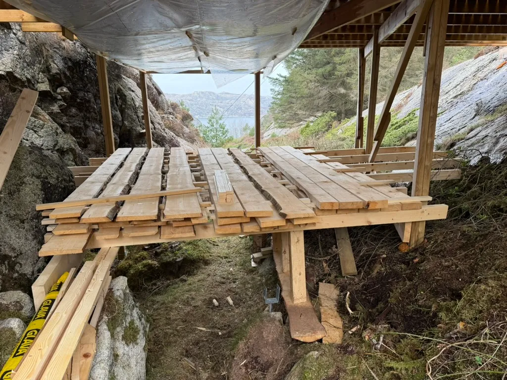 Fresh-sawn boards stickered with air gaps on a hillside drying platform, a fjord behind