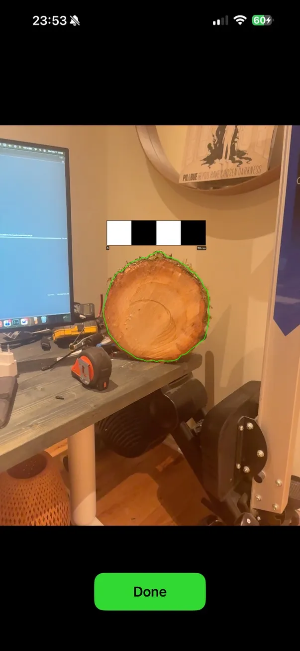 LogPlan on a phone outlining the end grain of a log against a scale bar, on a desk beside a developer's monitor